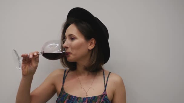 Κορίτσι δοκιμάζει ένα ποτήρι κόκκινο κρασί στο στούντιο. Μια γυναίκα πίνει κόκκινο κρασί σε λευκό φόντο. Μοντέρνο γυναικείο μοντέλο που καταπίνει αλκοόλ — Αρχείο Βίντεο