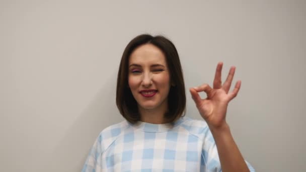 Female doing ok gesture in studio against white wall. Concept of approval and success. Young caucasian woman standing against white background and doing Ok sign with fingers — Stock Video