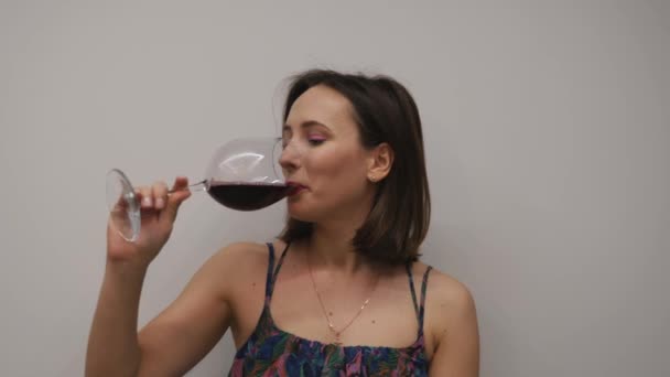 Mulher bebendo vinho tinto no fundo branco. Feminino millennial é degustação de copo de vinho tinto em estúdio — Vídeo de Stock