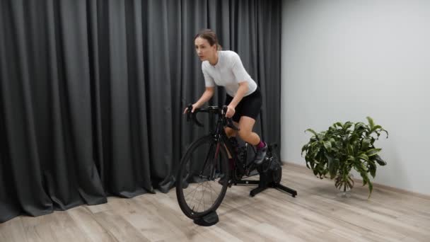 Ciclo dentro de casa em casa na mulher treinadora de bicicleta estacionária pedalando fora de sela como parte da preparação da corrida. Pro ciclismo — Vídeo de Stock