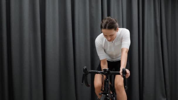 Graziosa acqua potabile femminile o bevanda isotonica mentre si pedala all'interno del ciclo smart trainer. Pedalata in bicicletta a casa allenamento fitness . — Video Stock