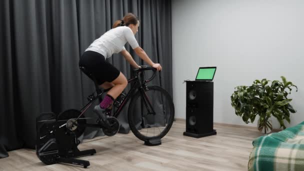 Kerékpáros nő okos edzővel. Fit kaukázusi női képzés kerékpár nézi a számítógépes képernyő versenyzés online. — Stock videók