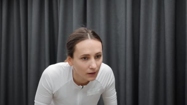 Treinamento de ciclo interno duro em bicicleta estacionária de treinador inteligente. Mulher focada no rosto enquanto faz exercícios de fitness em casa treinador de ciclismo em casa — Vídeo de Stock