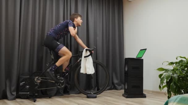 Mann schwitzt beim Radfahren auf Fahrrad Smart Trainer zu Hause. Männliche Feuchttücher mit Handtuch während des Indoor-Radtrainings. Junge Radfahrerin trainiert hart auf dem Rad — Stockvideo