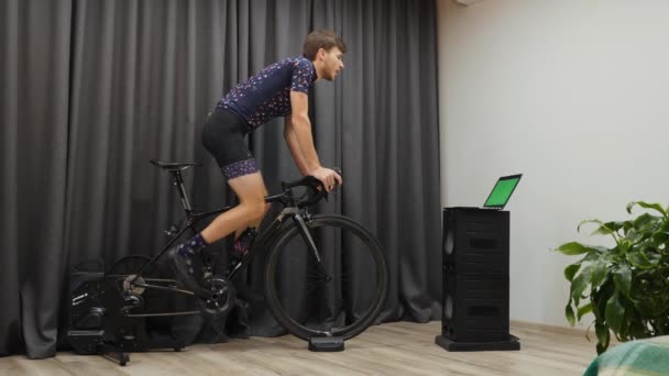 Professionell cyklist gör intervallträning på cykel smart trainer. Man trampar ur sadeln på hemma stationär cykel tränare. Begreppet cykling inomhus — Stockvideo