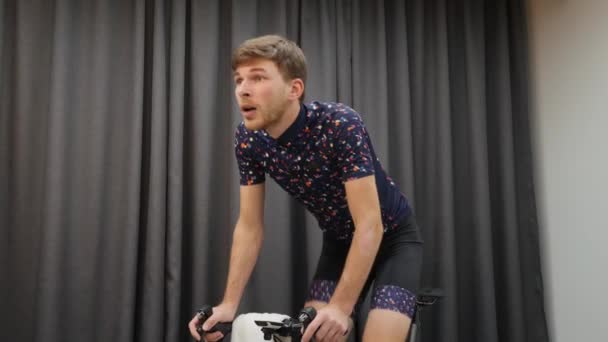 Male cycle out of saddle on bicycle smart trainer indoors. Sportive man intensively cycling and pedaling on home bike trainer. Young cyclist doing workouts on cycle at home — Stock Video