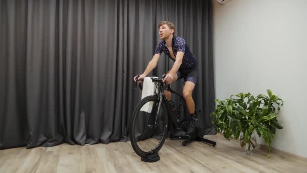Man cykla ur sadeln på smarta hem cykel tränare, dricka isoton eller vatten, bär professionella cykelkläder. Virtuell cykling inomhus — Stockvideo