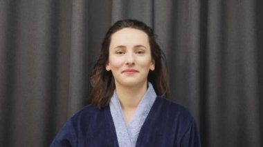 Kadın başındaki havluyu çıkarıp ıslak saçlara dokunuyor. Banyodan sonra ıslak saçlı, mavi bornozlu genç bir kadın. Sağlık ve güzellik