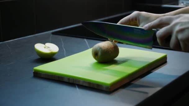 Beautiful female hands cutting green kiwi. Close up of womans hands cuts fruits on kitchen. Knife and chopping board. Healthy diet food — Stock Video