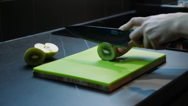 Une femme tranchant du kiwi. Jeune femme coupant kiwi vert au couteau sur planche à découper en plastique en bois, vue latérale rapprochée. Cuisine et concept alimentaire — Video