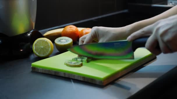 Mooie vrouwelijke handen snijden in plakjes fruit. Vrouw snijdt kiwi in de keuken. Gezonde voeding concept. Mes en snijplank. Close-up van handen snijden groene kiwi — Stockvideo
