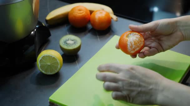 Kobieta obiera mandarynkę. Dłonie kobiety obierają mandarynki w kuchni, świeże owoce w tle. Kobieta przygotowuje koktajl owocowy. Organiczne zdrowe jedzenie. Koncepcja kuchni — Wideo stockowe