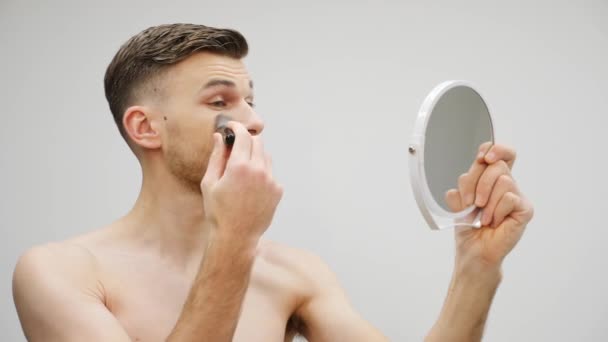男は化粧をする顔に化粧を施した若いハンサムな男。鏡を見ながらひげを生やしたゲイのメイク — ストック動画
