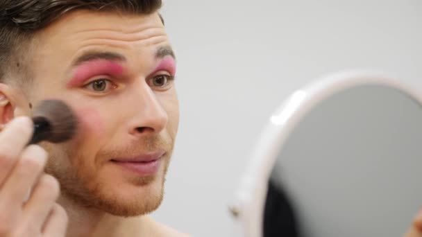 年轻的变性人自己化妆。 漂亮的男人用脸红在他的脸上。 旅行化妆的概念。 基佬的近视脸涂化妆品. — 图库视频影像