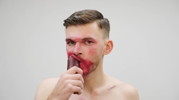 Bøsse mand spiser og nipper pølse. Portræt af transseksuel med smurt makeup bider af og sluge pølse, front view. Travesthy og transseksuel koncept – Stock-video