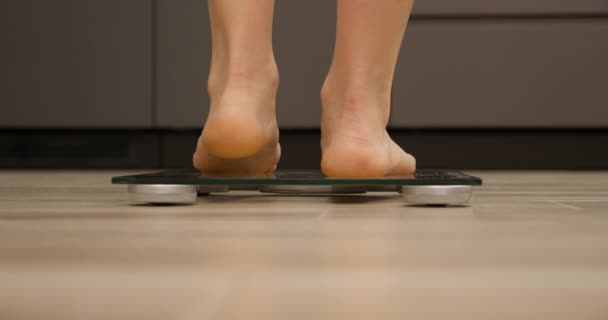 Pies de niña de pie sobre una balanza. Mujer en escamas. Comprobación de peso femenino o sobrepeso, primer plano, vista trasera — Vídeos de Stock