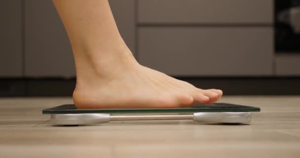 Feet stepping on weighing scales. Female barefoot measuring body weight in kitchen. Woman checking weight. Human legs on scales — Stock Video