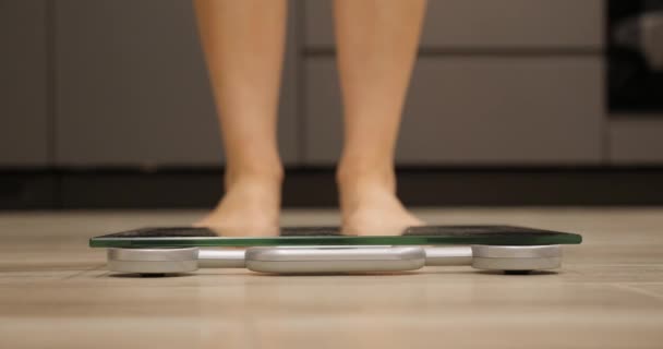 Una mujer descalza pisa escamas. Pies femeninos midiendo peso corporal. Piernas humanas en básculas de pesaje en la habitación. Chica chequeando su peso — Vídeos de Stock