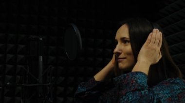 Genç bayan şarkıcı profesyonel kayıt stüdyosunda mikrofona şarkı söylüyor. Kulaklıklı bir kadın, müzik stüdyosunda şarkıyı kaydediyor. Ev müziği stüdyo konsepti
