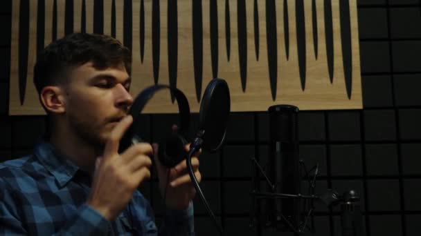 Músico en auriculares cantando al micrófono en el estudio de grabación. Cantante masculino profesional grabando la canción en el estudio de sonido en casa. Proceso de composición musical — Vídeos de Stock