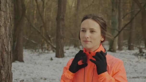 Una donna si mette le cuffie. Attraente giovane femmina si mette le cuffie prima dell'allenamento all'aperto. Atleta professionista in giacca arancione prima degli allenamenti. Concetto Run — Video Stock