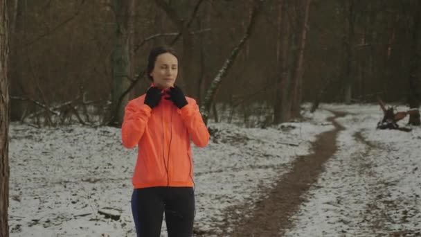 Female puts on headphones before training. Young confident woman in sports wear puts on headphones in park. Girl with beautiful sportive body putting on headphones before outdoor run training — Stock Video