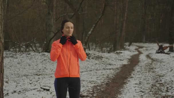 Kız kulaklık takıyor. Güzel spor vücutlu bir kadın kış parkında koşuya çıkmadan önce kulaklık takıyor. Parkta kulaklıklı bir kadın. Ormanda koşmaya hazırlanan bir sporcu — Stok video