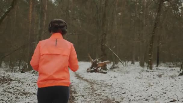 Frau joggt im Park. Hündin mit schönem, sportlichem Körper in orangefarbener Jacke läuft im Winterwald. Profi-Läufer bereitet sich auf Marathon in der Nebensaison vor. Junge Athletin trainiert hart im Freien — Stockvideo