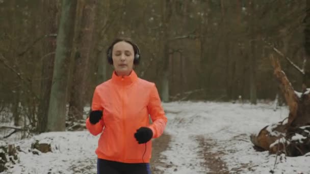 Mujer con auriculares corriendo en el parque. Atleta femenina motivada corriendo y entrenando duro por la mañana en el bosque de invierno. Corredor profesional preparándose para el campeonato de carreras trail run en temporada baja . — Vídeos de Stock