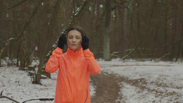 Kobieta zakłada słuchawki i zaczyna biegać w parku zimowym. Pewna siebie młoda kobieta biegająca i ćwicząca codziennie na świeżym powietrzu w lesie. Dziewczyna ciężko trening dla utraty wagi. Koncepcja przebiegu trasy — Wideo stockowe