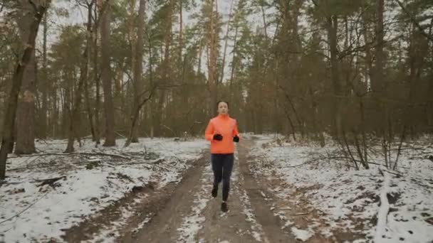 Mujer activa corriendo en el parque de invierno. Vista frontal de la joven atleta atractiva en ropa deportiva corriendo por la mañana. Corredor profesional duro entrenamiento al aire libre. Trail run y concepto deportivo — Vídeo de stock