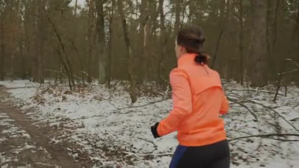 Kobieta biega po parku. Samica trenuje poza sezonem. Dziewczyna w pomarańczowej kurtce i niebieskich rajstopach biegających na świeżym powietrzu. Profesjonalny sportowiec przygotowujący się do maratonu i wykonujący ćwiczenia cardio workout. Bieg szlaku — Wideo stockowe