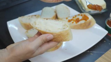 Kadın ekmeğin üzerine kırmızı havyar koyar. Havyarlı sandviç yapmaya yaklaş. Ev yemeği. Ekmeğe kırmızı havyar ve tereyağı koyma süreci
