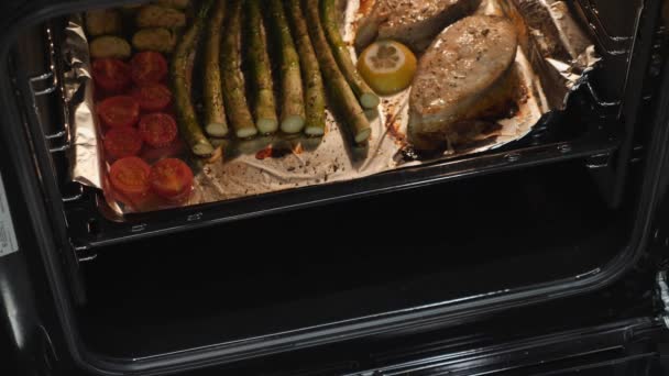 Detailní záběr pečeného lososového steaku a zeleniny. Vařené ryby a rajčata připravené v elektrické troubě. Zdravé stravování. Žena vyndá večeři z trouby. Domácí kuchyně — Stock video