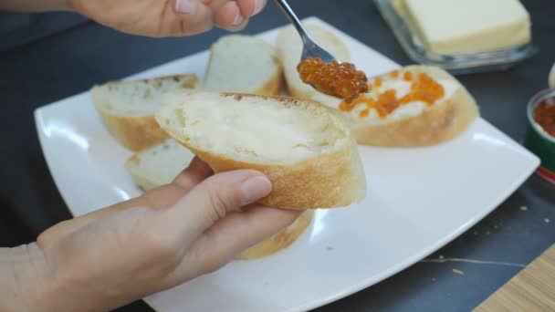 Woman puts red caviar on bread with spoon. Close up of sandwiches with butter and caviar. Home cooking. Woman spreads red caviar on canaps and puts on white plate — 비디오