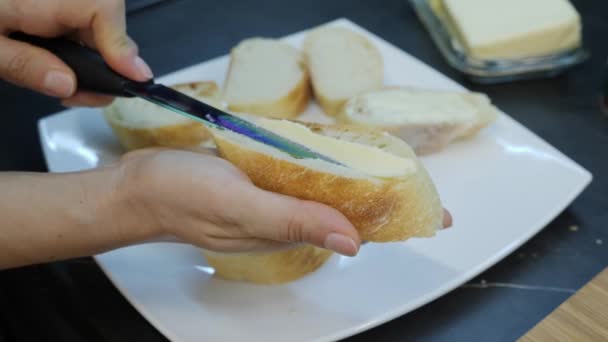 Mulher espalha manteiga no pão com faca. Chef esfrega manteiga em canapés. Close up de faca está espalhando margarina no pão branco. Cozinha caseira. Processo de fazer sanduíches — Vídeo de Stock