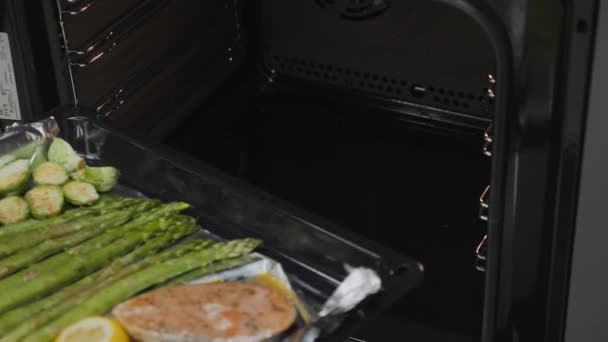 Chef starts grilling salmon seasoned with tomatoes,  Brussels sprouts and green asparagus in the oven. Slow motion. — 비디오