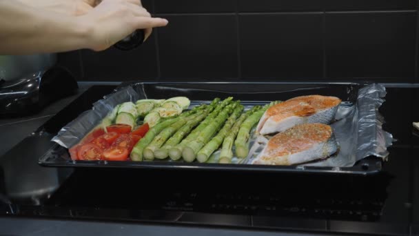 Шеф-повар приправляет свежие овощи и рыбу из форели специями перцем и солью перед приготовлением в духовке — стоковое видео