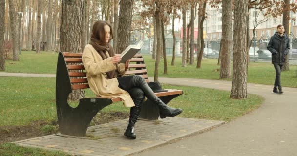 Frau sitzt auf Bank und liest ein Buch und Mann kommt zu ihr und beginnt eine lustige Geschichte zu erzählen, nach der sie zusammen lachen. — Stockvideo