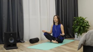 Lotus pozunda oturan ve kulaklıkla meditasyon müziği dinleyen bir kadın. Yoga minderinde oturan ve evde meditasyonun tadını çıkaran gözleri kapalı rahatlamış bir kadın. Farkındalık kavramı