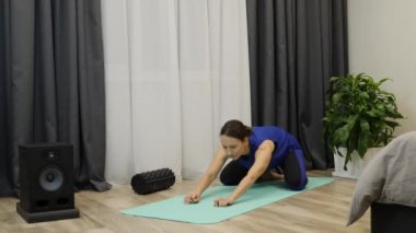 Kadın evde spor ve spor eğitimi alıyor. Klasik mavi bluzlu kadın, pantone blue leggins parlak odada paspas üzerinde egzersiz yapıyor. Yetişkin kız öne eğiliyor ve yoga minderinde geriniyor.