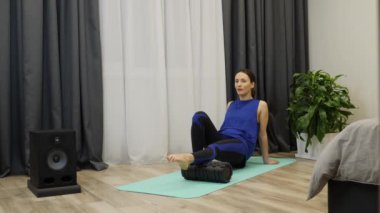 Female practicing myofascial release using fitness roller at home. Fitness teacher performs leg muscles massage after exercises training. Woman does restorative massage on yoga mat. Slow motion