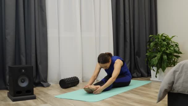 Femeia gimnastă se întinde acasă. Femeia sportivă stând pe covorul de yoga și practicând exerciții stretch. Bruneta caucaziană se încălzește înainte de lecțiile de yoga. Femeia care face exerciții de dimineață acasă — Videoclip de stoc