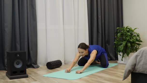 Femeia face sport și antrenament de fitness acasă. Femeie în top albastru clasic, pantone picioare albastre face exerciții pe mat în cameră luminoasă. Adult fata sprijinindu-se înainte și întinzându-se pe yoga mat — Videoclip de stoc