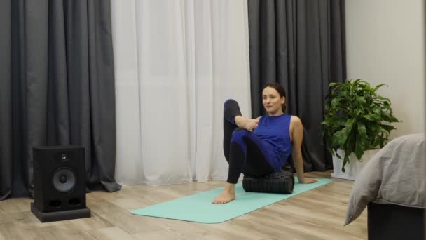 Woman doing rehab exercises and restorative massage using fascia fitness roller. Relaxed young female in blue sportswear massages body muscles using foam roller at home. Girl does relaxing exercises — 비디오
