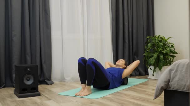 Gadis membuat latihan di kamar tidur tamu. Wanita memijat otot tulang belakang menggunakan rol untuk yoga. Instruktur kebugaran melakukan latihan rehabilitasi setelah latihan keras di rumah. Perempuan melakukan pijat dengan fascia roll — Stok Video