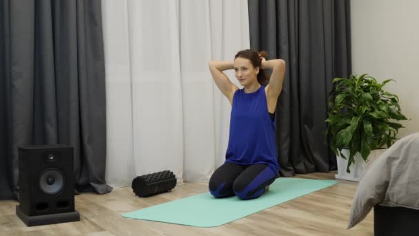 Feminino amarrando o cabelo em rabo de cavalo. Jovem mulher atraente em roupas esportivas azuis clássicas amarra o cabelo no rabo de cavalo antes de praticar ioga. Menina adulta sentada no tapete e se preparando para a meditação. Movimento lento — Vídeo de Stock