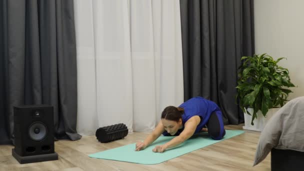 Female does sports and fitness training at home. Woman in classic blue top, pantone blue leggins doing exercises on mat in bright room.  Adult girl stretching on yoga mat. Slow motion — Stok video