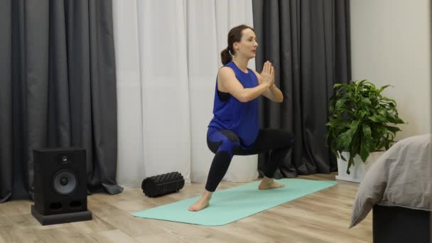 Meisje in kraakpositie op yogamat. Vrouw die yoga oefeningen doet. Vrouw in klassiek blauw topje en leggins die thuis fitnesstraining doet. Langzame beweging — Stockvideo
