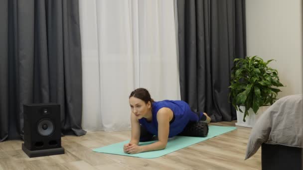 Woman stretches thigh muscles using yoga roller. Girl massaging frontal surface of leg after workout. Female does rehab and relaxing exercises using fascia roll. Slow motion — 图库视频影像